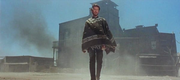 From "A Fistful of Dollars" 1964 Western, depicts "No Name" in front of a wooden building with a dust cloud.